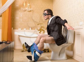 Man in pilot glasses sitting on the toilet bowl. Bathroom interior in retro style on background