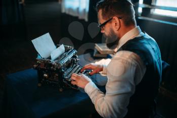 Portrait of bearded literature author in glasses typing on vintage typewriter. Creative people concept