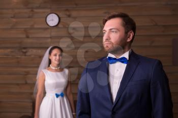 Serious groom in suit and happy bride in white dress, wooden background.