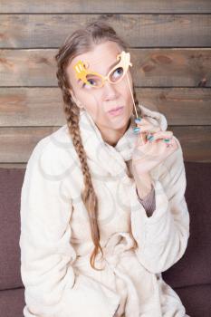 Young woman with yellow glasses on a stick, wooden background. Funny photo props. Fun accessories for shoots