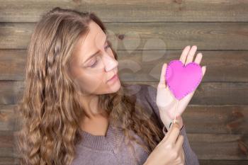 Young woman with funny pink heart in hand, wooden background. Fun photo props and accessories for shoots