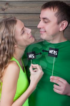 Portrait of happy love couple shows funny icons on a sticks with just married inscription, wooden background. Fun photo props and accessories for shoots