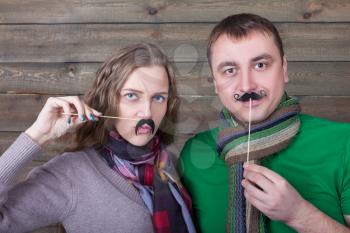 Cute couple with funny moustache on a sticks, wooden background. Fun photo props and accessories for shoots