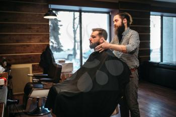 Bearded customer man in black salon cape visit barbershop. Coiffeur at work