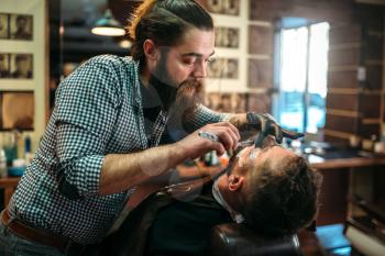 Barber shaves the beard of the client by shaving blade at barbershop. 