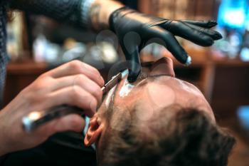 Barber shaves the beard by straight razor at barbershop. 
