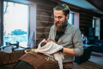 Barber wiping the client beard with a towel, barbershop interior on background. 