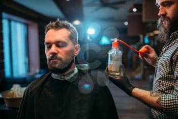 Barber splashing client face by aftershave lotion, barbershop interior on background. 