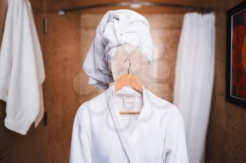 Woman with invisible face in bathrobe and hanger standing in bathroom. 