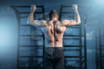 Strong sportsman training on horizontal bar in gym, back view. Muscle athlete on workout