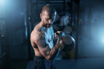 Muscular man exercises with kettlebell on training in gym. Strong athlete workout with weight 