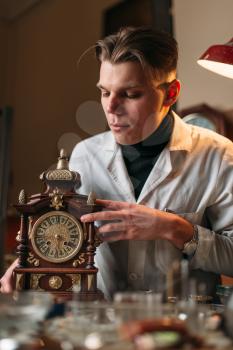 Watchmaker with old mechanical desk clock. Hour workshop