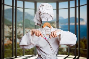 Woman with invisible face in bathrobe and hanger holding toothbruch and toothpaste in hands, coast on background. Personal hygiene advertising or marketing concept. Girl brushing teeth, invisibility e