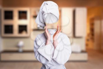 Woman in bath clothes with towel on head trying to touch her invisible face. Invisibility fantasy concept, transparent female person