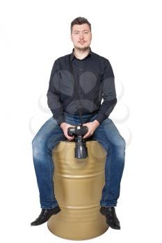 Photographer with digital camera sitting on an iron barrel, white background