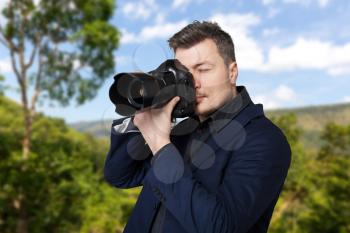 Professional photographer with digital photo camera takes the picture, green nature on background