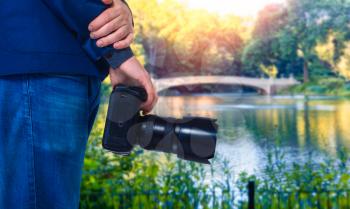 Male cameraman hands with digital camera, closeup, green nature and lake on background
