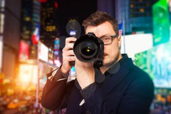 Portrait of male photographer in glasses with digital camera, front view, night cityscape on background