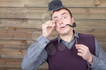 Young male with funny hat and smoking pipe on a sticks in hand, wooden background. Fun photo props and accessories for shoots