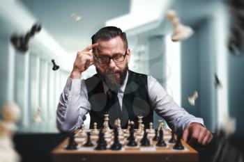 Pensive male chess player in glasses calculate movies and game strategy against chessboard. Figures flying around chessplayer. Intelligence competition concept