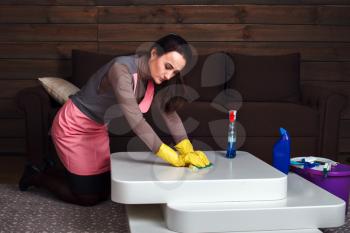 Young woman in uniform and rubber gloves cleans the table. Cleaning servisce concept