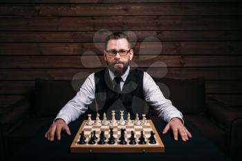 Male player in glasses sitting against the chess board with the pieces set. Strategy game concept