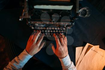 Male hands typing on retro typewriter, top view. Dark blue table cloth on background. Writer, journalist, literature author, blogger or poet concept