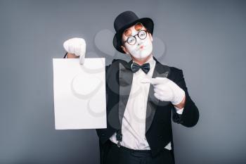 Male mime actor with empty paper sheet. Pantomime in suit, gloves, glasses, make-up mask and hat. April fools day concept
