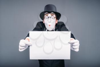 Pantomime actor with empty paper sheet. Mime artist in suit, gloves, glasses, make-up mask and hat. April fools day concept