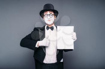 Pantomime actor performing with empty paper sheet. Comedy mime artist in suit, gloves, glasses, make-up mask and hat