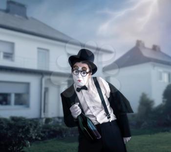Mime actor with big bottle of alcohol performing a drunk man. Comedy pantomime artist in suit, gloves, glasses, make-up mask and hat