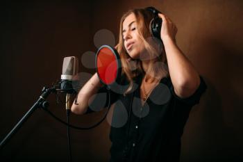 Female singer in headphones against microphone, song record in music studio. Woman vocalist . Audio recording. Professional digital sound technologies