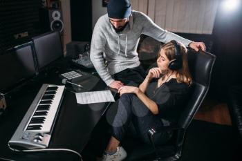 Female singer in headphones listen to song record against sound producer in music studio. Professional digital audio recording
