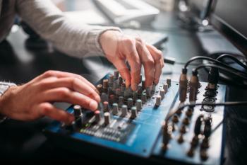 Male sound engineer hands on volume control panel. Digital music record studio. Professional audio engineering