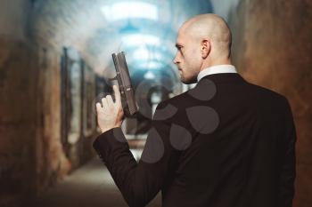 Contract killer with gun wallpaper concept, back view. Bald assassin in suit holds pistol in hand. Secret agent on mission