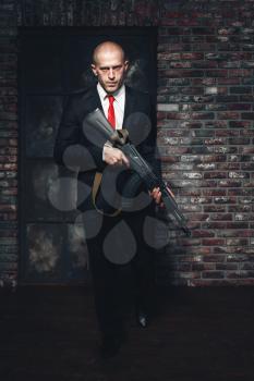Assassin in suit and red tie holding machine gun in hands. Contract murderer wallpaper, background or poster concept.