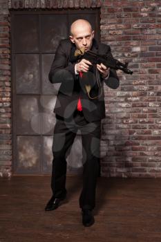 Assassin in suit and red tie holding machine gun in hands. Contract murderer wallpaper, background or poster concept.