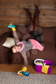 Playful woman in cleaning servisce uniform and rubber gloves poses on a couch. Housekeeping concept