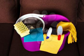 Cleaning servisce supplies in a busket, closeup, brown couch on background. Housekeeping business concept