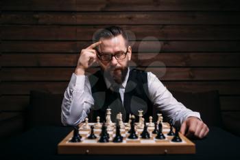 Pensive male chess player in glasses thinking about game strategy. Intelligence competition concept