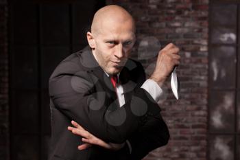 Silent killer, oriental martial arts in action. Bald contract murderer in suit and red tie holds combat knife. Fighting knife is a dangerous weapon in right hands