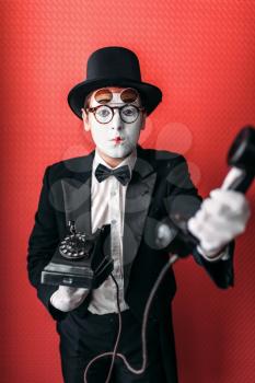 Mime theater actor performing with old telephone. Comedy pantomime artist in suit, gloves and hat