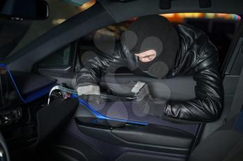 Carjacker unlock glove box with crowbar. Male thief with balaclava on his head hack car. Carjacking danger concept. Auto transport crime