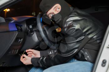 Male car thief breaks the ignition switch. Carjacker with balaclava on his head hack car. Carjacking danger concept. Auto transport crime. Vehicle insurance advertising 