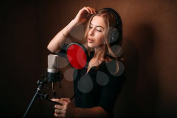Female singer recording a song in music studio. Woman vocalist in headphones against microphone. Audio recording. Professional digital sound technologies