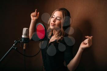 Happy woman vocalist in headphones against microphone, song record in music studio. Female singer recording audio track. Professional digital sound technologies