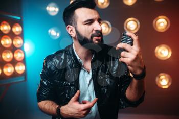 Brutal bearded performer with microphone sing a song on the stage with the decorations of lights