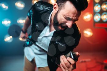 Brutal bearded performer with microphone sing a song on the stage with the decorations of lights