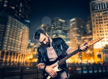 Male brutal performer with electric guitar against night cityscape