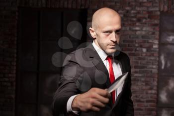 Silent killer, oriental martial arts in action. Bald contract murderer in suit and red tie holds combat knife. Fighting knife is a dangerous weapon in right hands